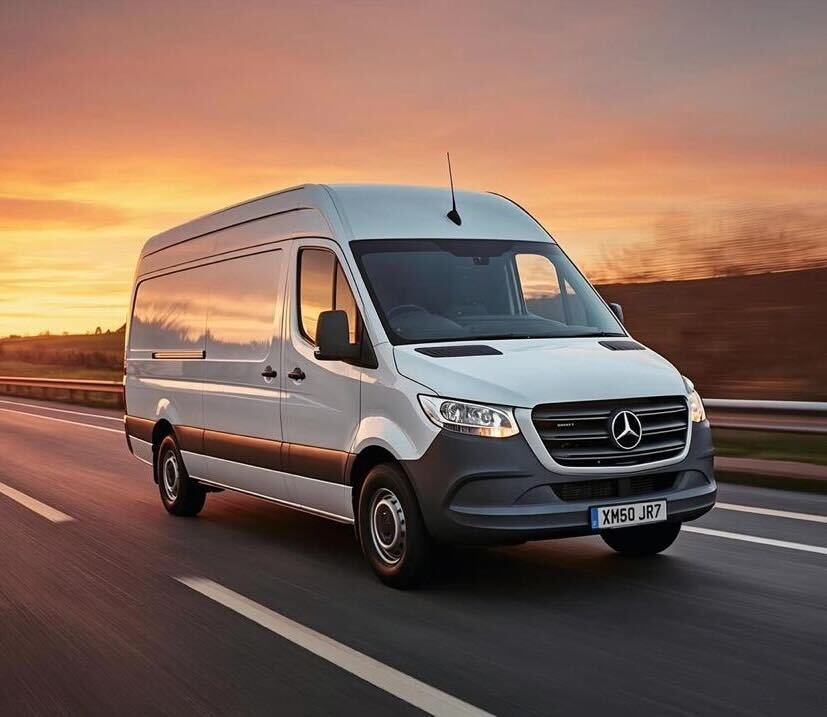 A white delivery van driving quickly on a highway during the day.